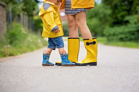 Mother and toddler child, boy, playing in the rain, wearing boots and raincoats
