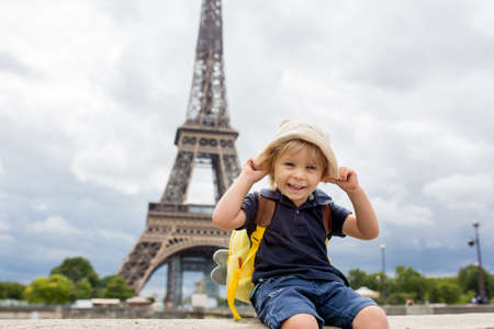 Happy blond toddler child, boy, visiting Paris during the summer, standing in front of the Eiffel tower, daytimeの写真素材