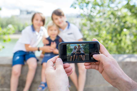 Happy children, boy brothers, visiting Paris during the summer, dad taking picture of them with phoneの写真素材