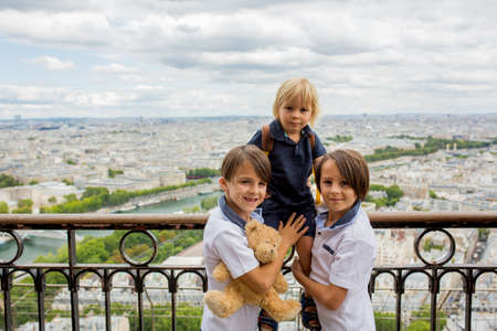 Happy children, boy brothers, holding teddy bear on top of the Eiffel tower, looking at the city, visiting Paris during the summerの写真素材
