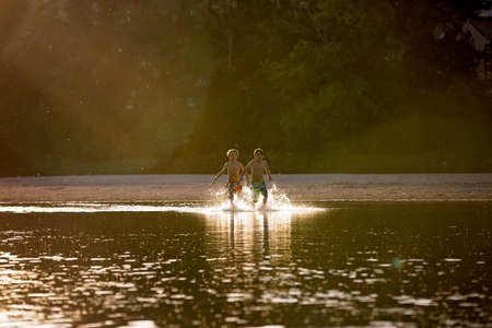 Beautiful portrait of children in lake, kids playing in the water on sunset, summertimeの写真素材