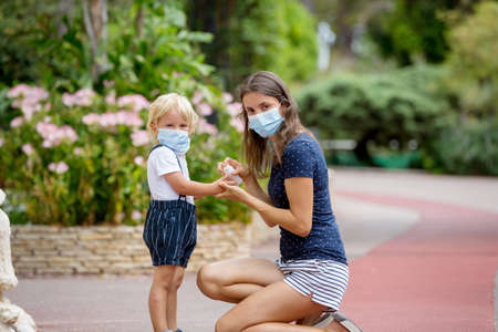 Mother and child, boy and mom, wearing masks and using disinfection outdoorsの写真素材