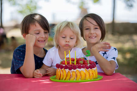 Sweet little blond toddler boy, celebrating his third birthday in a park, outdoors