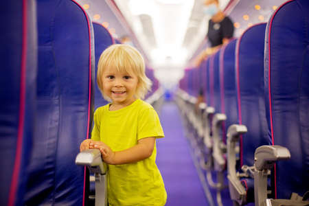 Toddler boy, child boarding on the airplane, standing on the aisle between the rows of seats, smiling happilyの写真素材