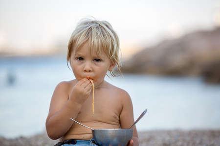 Cute boy, child, eating spaghetti on the beach, enjoying dinner outdoorsの写真素材