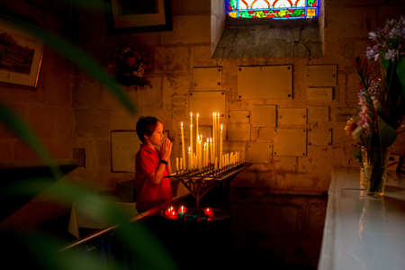 Little toddler boy, praying in chapel with candles in front of him