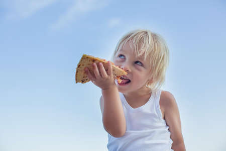 Sweet toddler child, eating pizza on the beach, having fun, smiling happily, kid enjoying dinner at the beachの写真素材