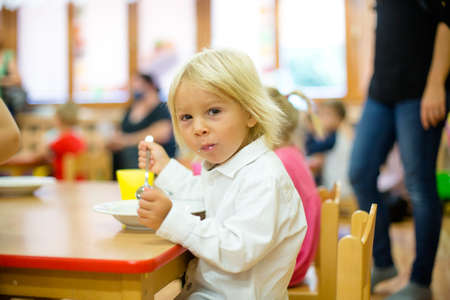 Blond toddler child, eating breakfast in kindergardenの写真素材