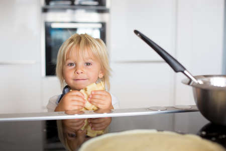 Cute toddler child, blond boy, making pancake in kitchen, eating themの写真素材