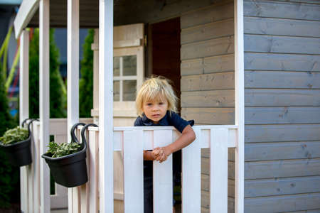Sweet toddler boy, playing in wooden doll house in garden, looking outの写真素材
