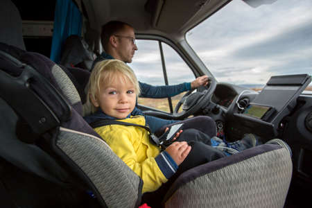 Cute toddler boy, kid sitting on the front seat in child seat on big camper van, smiling happilyの写真素材
