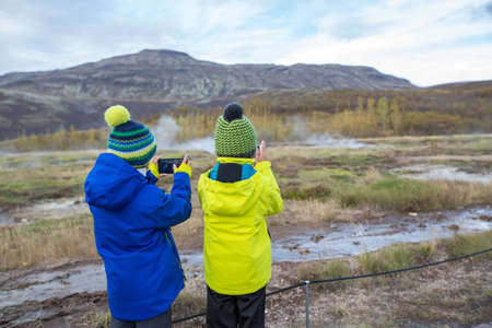 Children, taking picture of Strokkur Geysir while erupting, Iceland autumntime