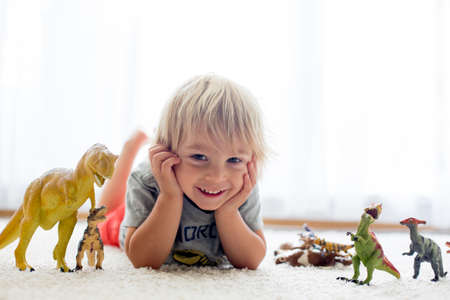 Blond toddler child, playing with dinosaurs at home, nice soft back lightの写真素材