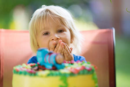 Toddler boy, celebrating his birthday with colorful cake outdoors