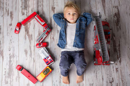 Child, toddler blond boy, playing with fire trucks on the floor at home