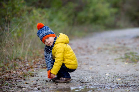 Cute toddler child with yellow jacket, running in autumn park, playing and jumping happily