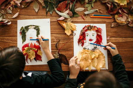 Child, creating woman portrait of leaves in living room, applying leaves using glue, autumntimeの写真素材