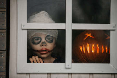 Scary toddler child in halloween costume, playing with carved pumpkins and candlesの写真素材