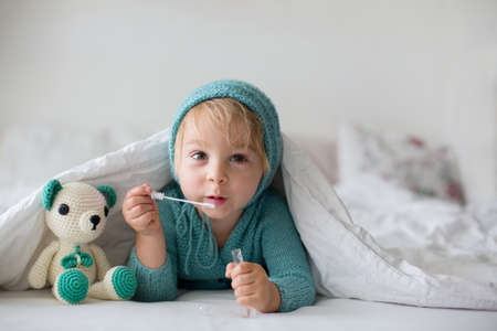 Cute toddler boy with handmade knitted toy, lying in bed, smiling happilyの写真素材