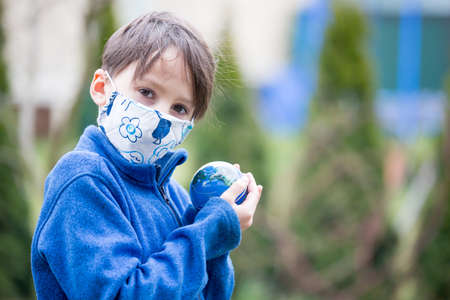 School child, holding small globe, looking sad at the world during Covid 19 pandemic, virus that spread worldwideの写真素材