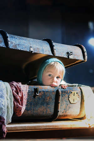 Little child, boy, hiding in old vintage suitcase in the attic, scared not to be foundの写真素材