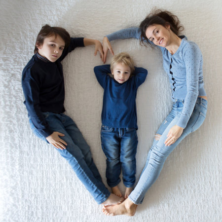 Beautiful family picture of mother and two children, making heart shape, lying on the bed and...