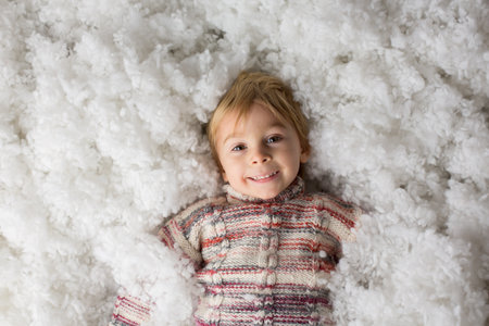 Cute toddler child, holding knitted toy, playing in the snow with colorful snowmen, smiling happilyの写真素材