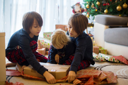 Happy children, boys, opening presents on christmas day, dressed in pajamasの写真素材