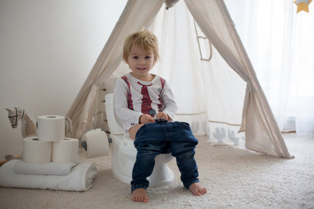 Cute toddler child, boy, sitting on a baby toilet potty, playing with toysの写真素材