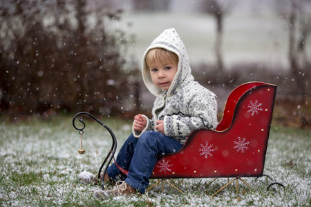 Beautiful blond toddler child, boy, with handmade knitted sweater playing in the park with first...