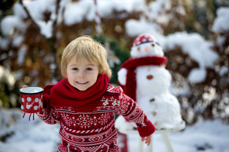 Sweet blond toddler child, boy, playing in garden with snow, making snowman, happy kid winter time outdoorsの写真素材