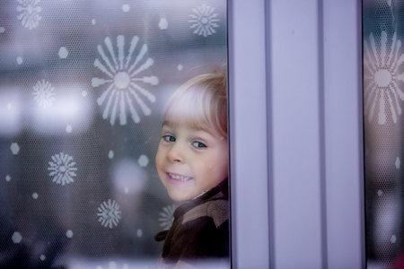 Little toddler boy, sitting behind the window, looking outsideの写真素材