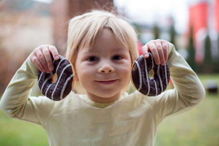 Sweet toddler child, playing with chocolate donuts, eating them happilyの写真素材
