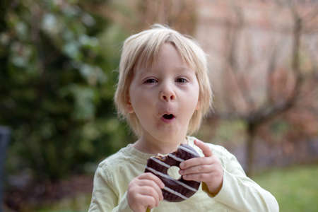 Sweet toddler child, playing with chocolate donuts, eating them happily