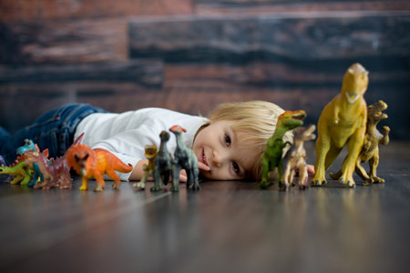 Blond toddler child, playing with dinosaurs at home, nice soft baclk lightの写真素材