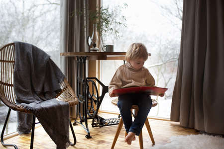 Cute toddler child in a little fancy wooden cottage, reading a book, drinking tea and enjoying cozy atmosphereの写真素材