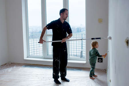 Cute toddler child, painting wall in new home with fatherの写真素材