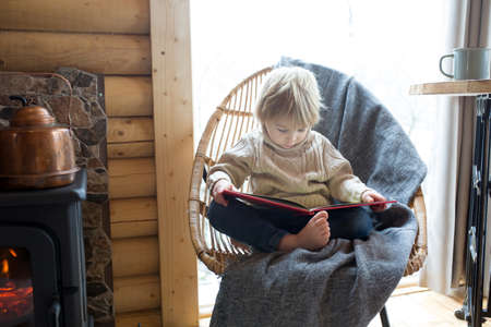 Cute toddler child in a little fancy wooden cottage, reading a book, drinking tea and enjoying cozy atmosphereの写真素材