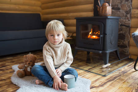 Cute toddler child in a little fancy wooden cottage, reading a book, drinking tea and enjoying cozy atmosphereの写真素材