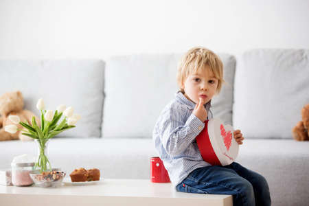 Beautiful blond boy, giving mother flowers and box with little gift for mothers day at sunny living roomの写真素材