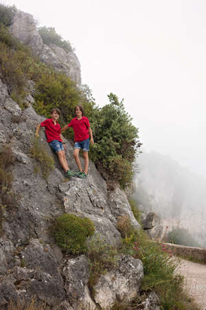 Children, boy brothers, standing on a big rock over a precipice on a walk summertime, high in the...