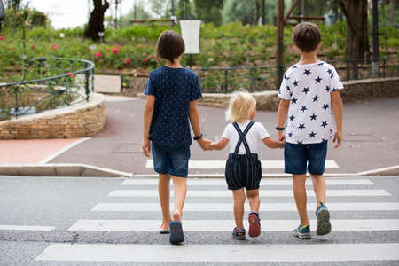 Children, boy brothers, siblings holding hands and crossing crosswalk on the street, summertime