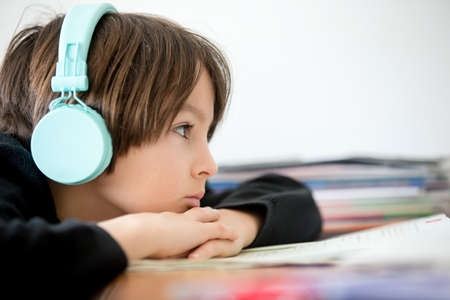 Sad school child, struggling with studying, sitting at the table with laptop, writing school tasks...
