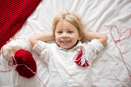 Cute child, blond boy, playing with white and red bracelet, called Martenitsaの写真素材