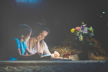 Beautiful mom and preschool boy, reading a book in the attic, nice atmosphere, flowers and strawberries next to himの写真素材