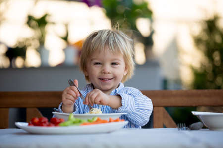 Cute child, blond toddler boy, eating spaghetti in garden summertimeの写真素材