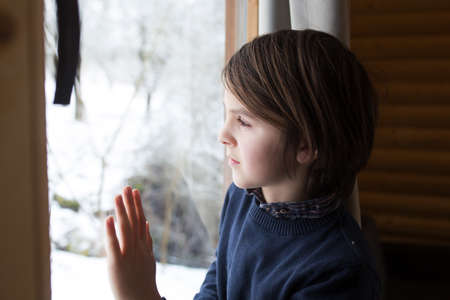 Beautiful preteen child in a little fancy wooden cottage, looking out of the window and enjoying...