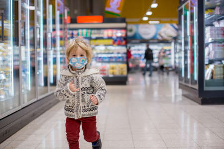 Cute toddler child, boy, wearing medical mask in supermarket store during covid pandemic lockdownの写真素材