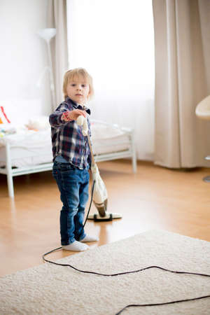 Cute little toddler child, boy, vacuum cleaning in living roomの写真素材