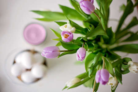 Beautiful vase with white and purple tulips on a table with candle and easter eggs, blurred in the backgroundの写真素材